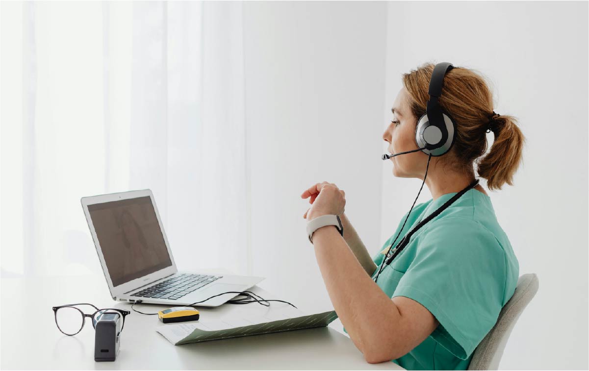 Doctor with over the ear headset having a video call with a patient on her laptop